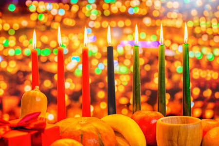 Kwanzaa celebration concept with seven candles red, black and green, gift box, pumpkin, bowl and fruit on light blur bokeh background, close upの写真素材