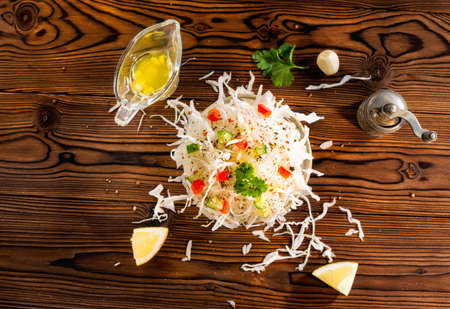 flat lay of white cabbage in bowl decorated red pepper, cucumber, garlic and parsley, lemon, grinder, olive oil over wooden table, concept healthy lifestyleの写真素材