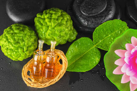 top view of spa concept bergamot, leaf, fragrance oil, lotus and zen basalt stones with water dew on black background, close upの写真素材