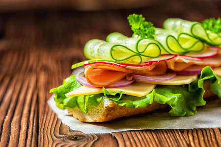 Close up of sandwich with ham, cheese, bacon, radish, lettuce, cucumbers and onions on paper, wooden backgroundの写真素材