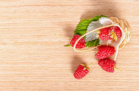 top view of red ripe raspberries scattered from basket to wooden table, close upの写真素材
