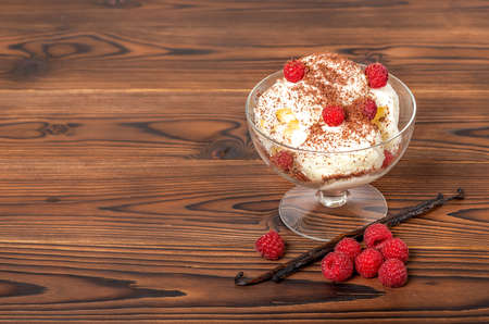 sweet dessert raspberry pink ice cream scoops with sprinkled chocolate, vanilla pod and fresh raspberry on wooden tableの写真素材