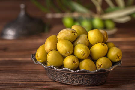 pickled green olives in plate lie on wooden background decorated branch of olive tree and grinder, arab styleの写真素材