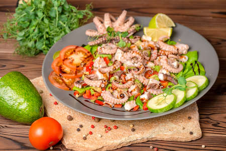 salad with tentacles of octopus, lime, avocado and lettuce, decorated lime, avocado, tomato, sprigs of pea leaves and dry peppers, natural seafoodの写真素材