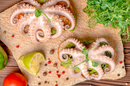top view of sandwiches with octopus and bread toast decorated lime, avocado, tomato, sprigs of pea...