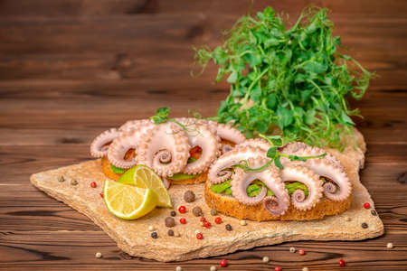 sandwiches with octopus and bread toast decorated lime, bunch of sprigs pea leaves and dry peppers on stone background, natural seafoodの写真素材