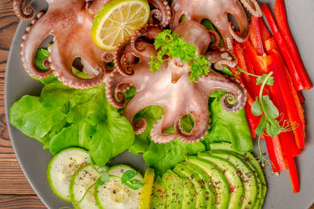 top down of octopus served with sliced avocado, lettuce, red pepper, lime, cucumber and sprig of pea leaves on plate, restaurant foodの写真素材
