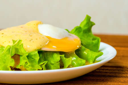 Closeup poached eggs, ham, lettuce leaf and delicious buttery fresh hollandaise sauce on toasted English muffin. Eggs Benedictの写真素材