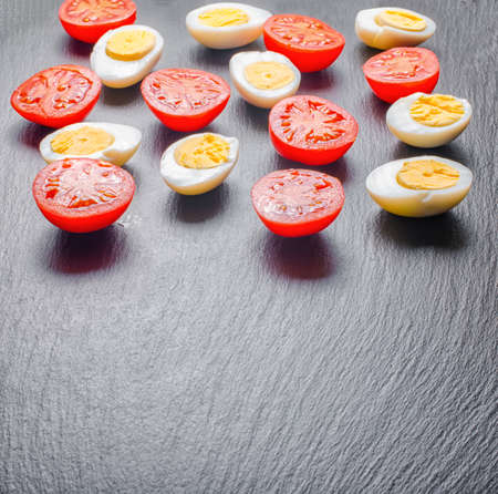 Beautiful red tomatoes cherry and half chicken eggs on black slate background with copy space, close upの写真素材