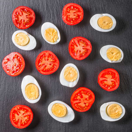 Top view of beautiful pattern red tomatoes cherry and half chicken eggs on black slate background, close upの写真素材