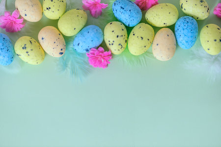 flat lay of multi colored painted Easter eggs, feathers and spring flowers over green, holiday...