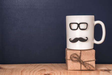 cup with mustache, glasses, gift box over black chalkboard, holiday concept of Fathers Day の写真素材