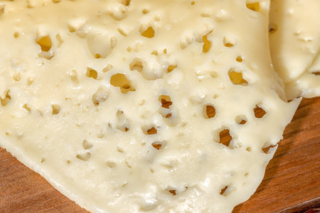 close up of holes cheese sliced on wooden texture, dairy product 