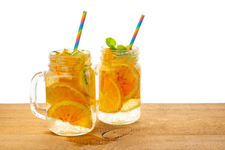 jars of homemade lemonade with sliced fresh lemon, orange, lime, twig mint, bubbles and straws on wooden background isolated, concept of refreshing summer drinkの写真素材