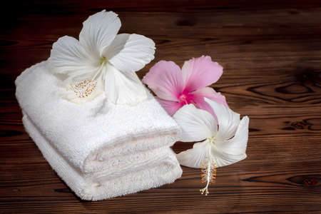 White cotton towels folded and flowers of hibiscus on wooden background, close upの写真素材