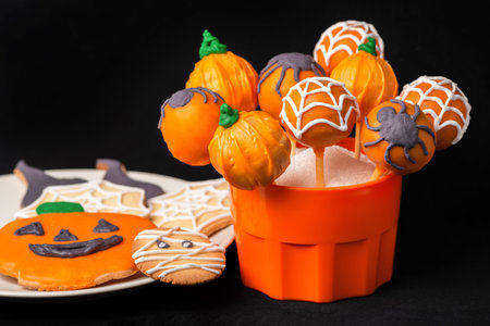 festive glazed cake pops and cookies decorated spider web isolated over black background, concept of Halloween partyの写真素材