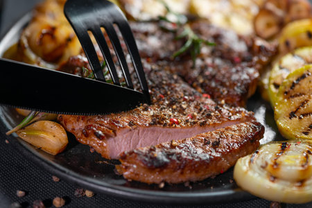 cutting with knife and fork delicious grilled wagyu beef roast with vegetable on black plate
