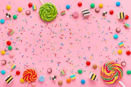 festive wreath background with assortment of colourful caramel candies, lollipops and sprinkles over pinkの写真素材