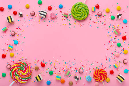 festive wreath background with assortment of colourful caramel candies with jelly and sprinkles over pink and space for your greetingsの写真素材