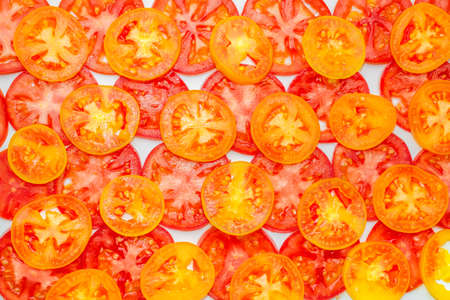 trendy pattern of thin sliced ripe red, yellow and orange tomatoes on white background, healthy natural food backgroundの写真素材