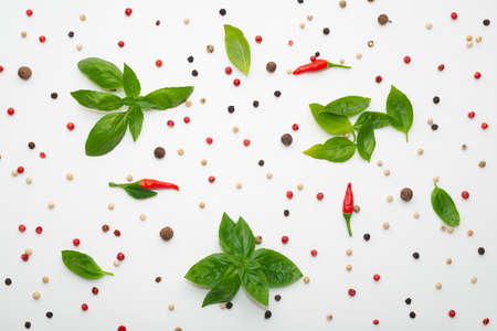flat lay of green basil leaves and black, red peppers on white backgroundの写真素材