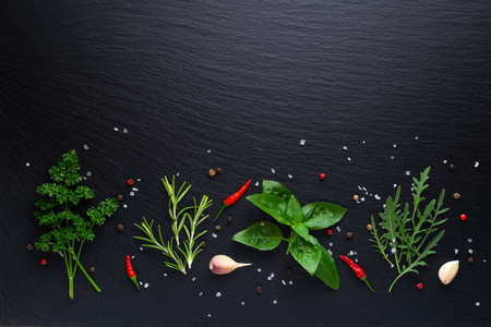 top down of arugula, rosemary, basil and parsley with spices on black slate with copy spaceの写真素材