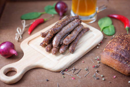 Grilled beef sausages, vegetables, spices and beer on the plywood backgroundの写真素材