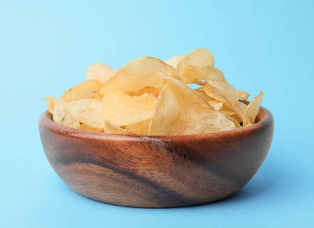 Wooden bowl with tasty potato chips on light blue background, closeupの写真素材