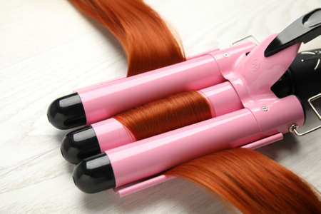 Triple barrel curling iron with red hair lock on light background, closeupの写真素材