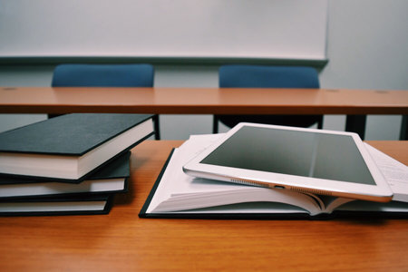 Textbooks and tablet computer on wooden desk in classroom closeup. Modern education conceptの写真素材