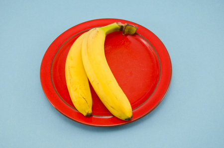 two yellow banana in red plate on azure background