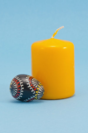 painted wooden easter egg and yellow candle on azure backgroundの写真素材