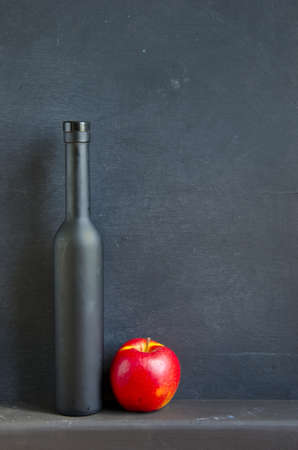 black bottle and red apple on black wooden backgroundの写真素材