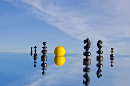 black chess pieces and yellow billiards ball on mirror in spaceの写真素材