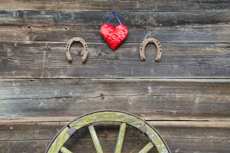 carriage wheel and horseshoe with red  heart on old wooden farm wallの写真素材