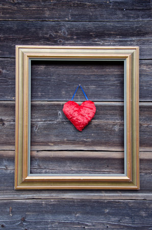 golden picture frame on old wooden wall and red heart symbolの写真素材