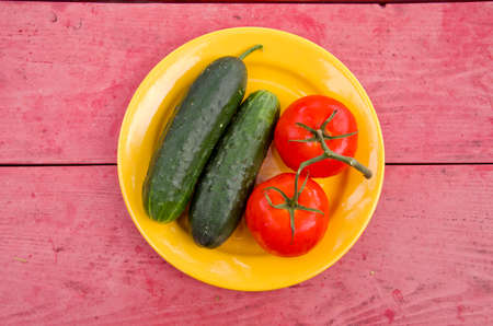 fresh tomato ond cucumber in yellow plate on red garden tableの写真素材