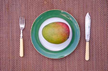 ripe mango fruit in plate with fork and knife
