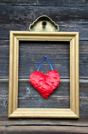 vintage golden picture frame with red heart on old wooden wallの写真素材