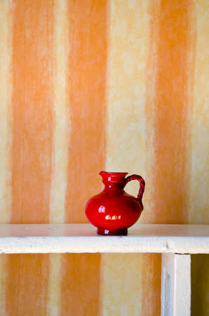one red ceramic jug on white wooden shelfの写真素材