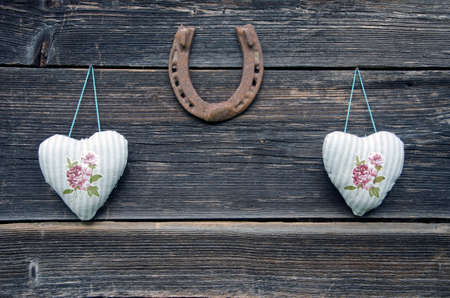 textile cloth hearts on old wooden wall and rusty horseshoeの写真素材
