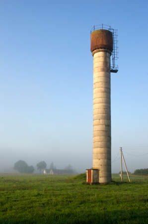 rural foggy early morning landscape with concrete old water towerの写真素材