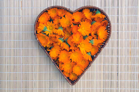 marigold calendula medical flowers in heart form wicker basket on tableclothの写真素材