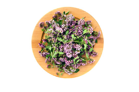 wooden ecological plate with fresh wild marjoram medical flowers isolated on whiteの写真素材