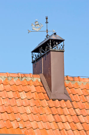 decorative ornamental chimney smokestack on tile roof with metal weathercockの写真素材