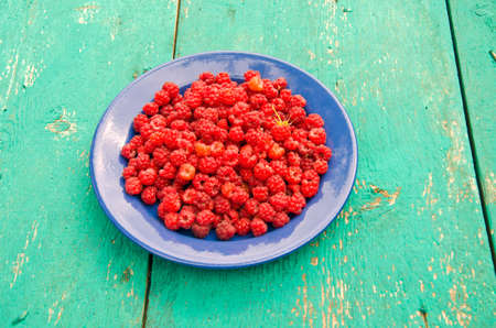 fresh sweet summer raspberry in blue ceramic plate on wooden tableの写真素材