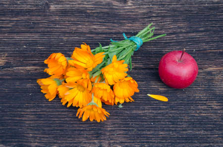 medical calendula marigold flower bunch and red apple on old wooden plankの写真素材