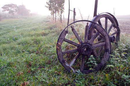 Sunrise on foggy autumnal landscape with two antique horse carriage wooden wheelsの写真素材