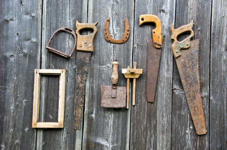 Many rusty vintage carpentry tools and horseshoe hanged on old wooden wall