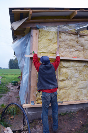 Farm worker insulating wooden house wall with mineral rock woolの写真素材